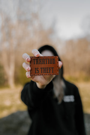 person holding a brown leather patch that says taxation is theft 