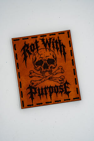 Rot with Purpose leather morale patch: skull and crossbones with Rot With Purpose in metal-style lettering, light brown leather, hand sewn with black thread and hook backing