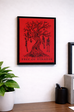Framed artwork titled 'Tree of Tyrants' on a wall with a plant and desk in the foreground.